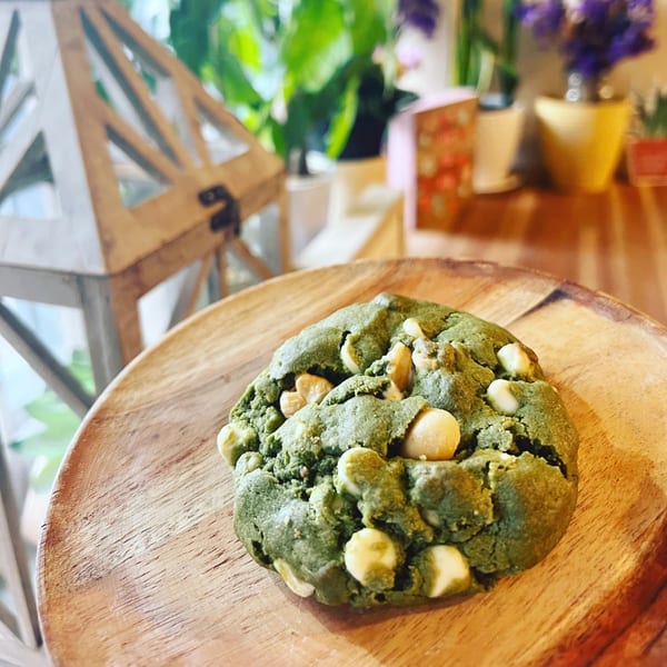 A green matcha cookie with white chocolate chips on a wooden plate at Morning Talk Cafe.