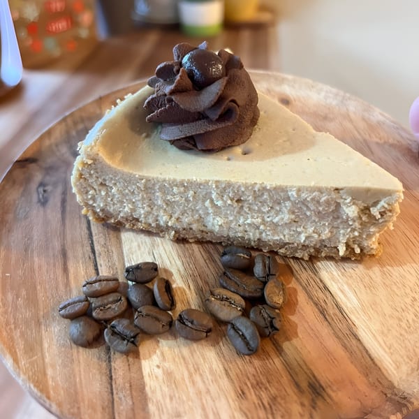 A slice of coffee cheesecake with chocolate whipped cream and coffee beans on a wooden plate.
