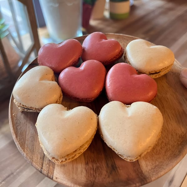 Heart-shaped macarons, some pink and some cream-colored, arranged on a round wooden tray.