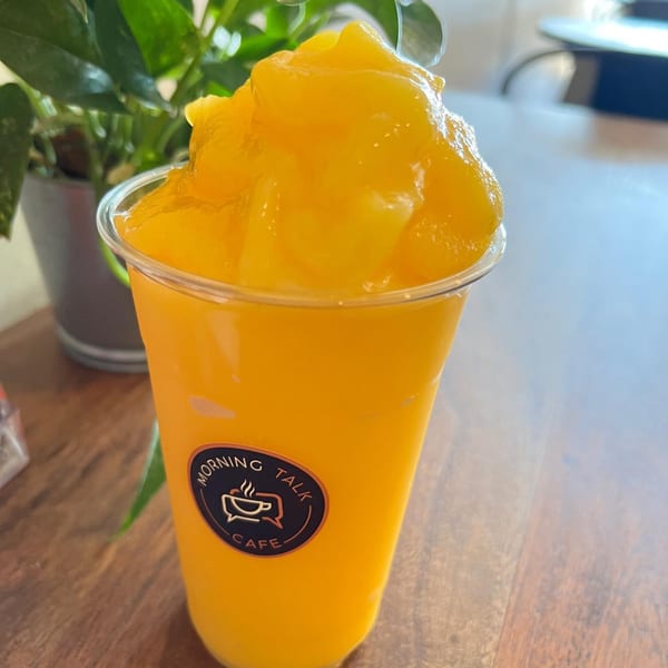 Morning Talk Cafe's vibrant yellow mango smoothie with a domed top, on a wooden table.