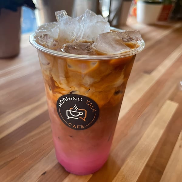 Iced coffee drink with pink and brown layers, Morning Talk Cafe logo, on a wooden table.