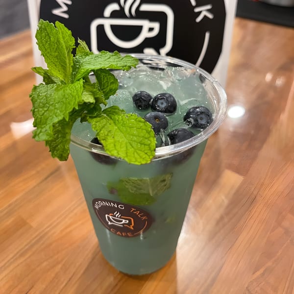 Morning Talk Cafe's blue drink with blueberries, ice, and fresh mint on a wooden table.