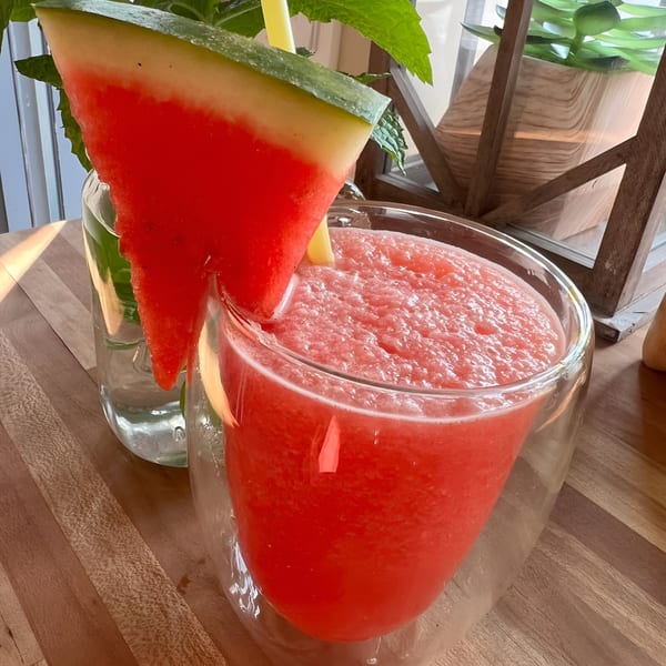 A Morning Talk Cafe watermelon smoothie with a watermelon slice and straw, on a wooden table.