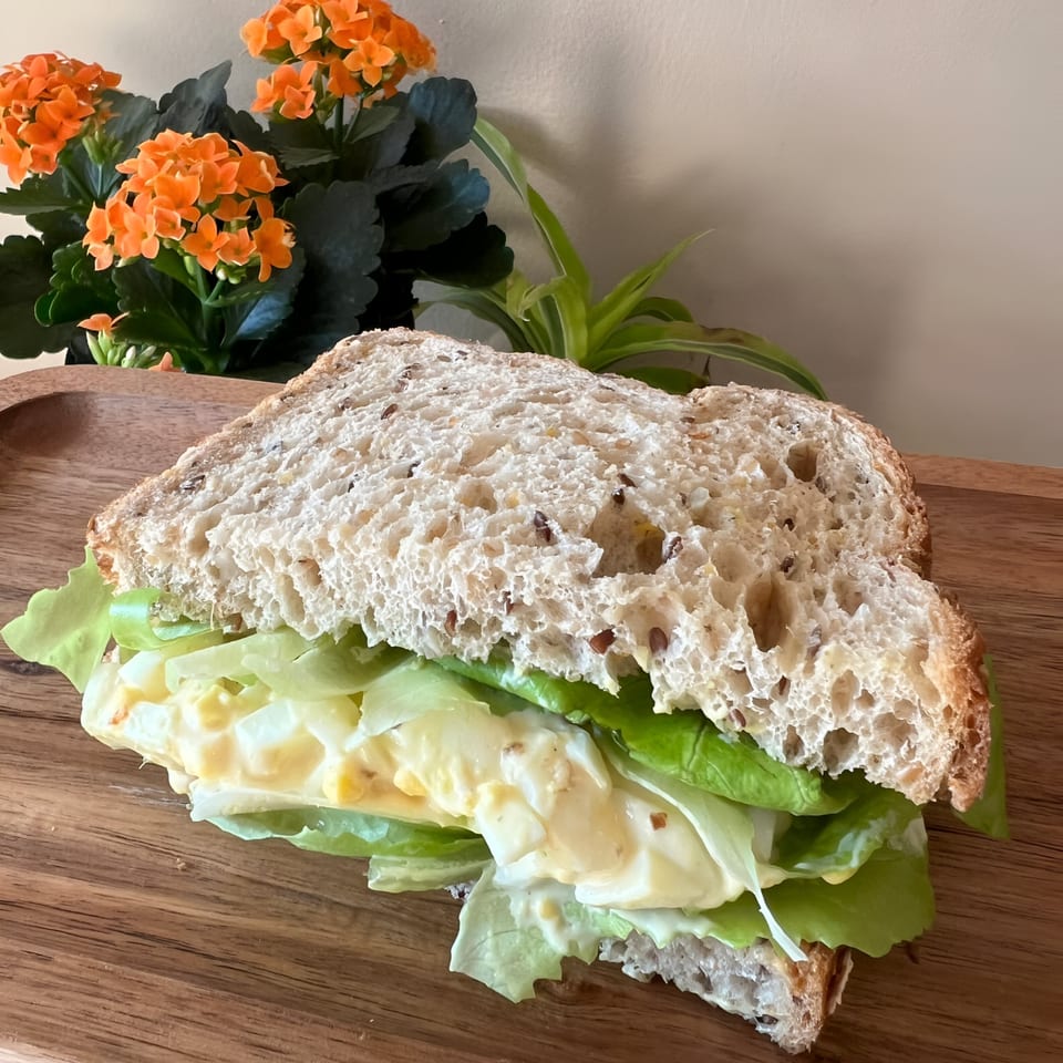 Morning Talk Cafe's egg salad sandwich on whole grain bread with lettuce, on a wooden board.