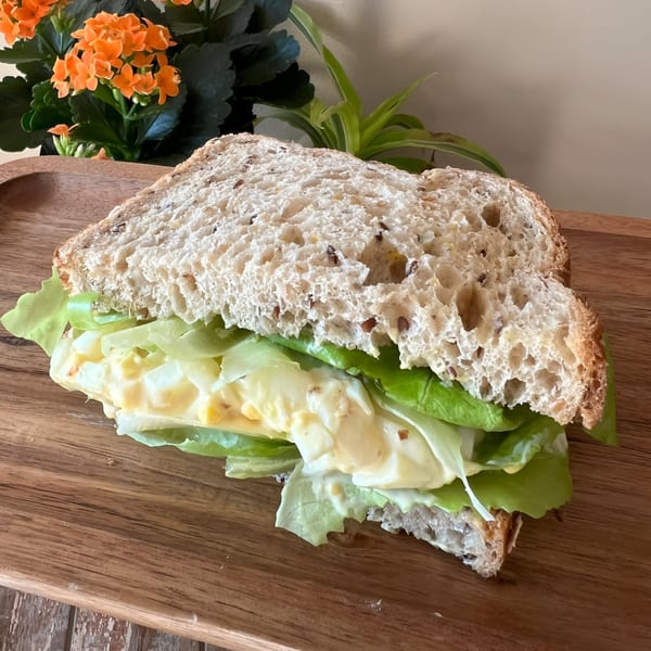 Morning Talk Cafe's egg salad sandwich on whole grain bread with lettuce, on a wooden board.