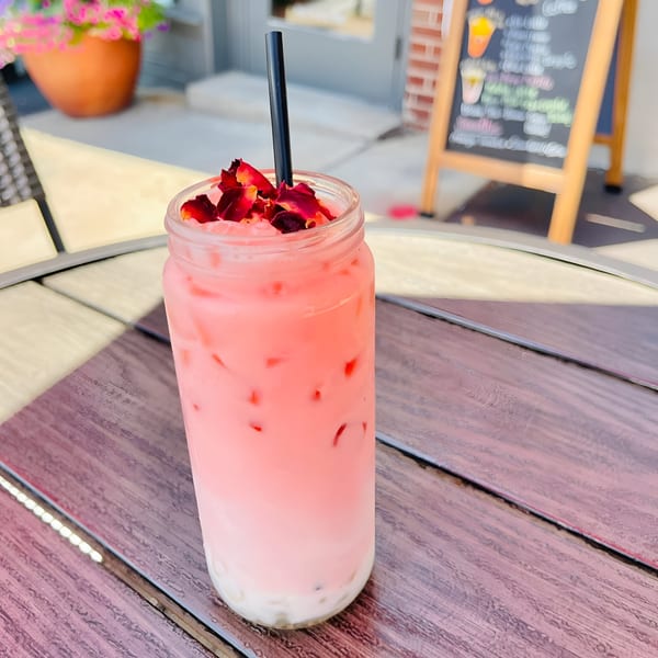 Pink layered drink with rose petals and a black straw on a wooden table at Morning Talk Cafe.