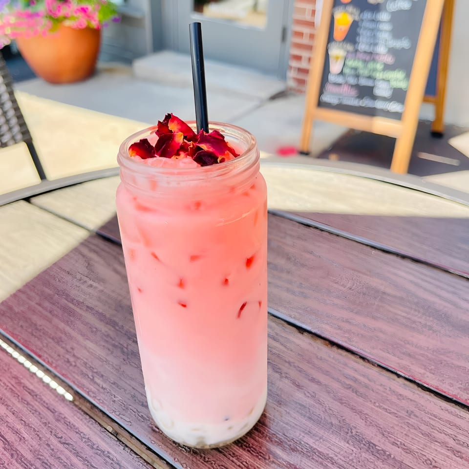 Pink layered drink with rose petals and a black straw on a wooden table at Morning Talk Cafe.